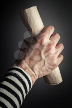 Strong sailor hand holds rolled old crumpled paper sheet over black background, secret pirate map  concept. Vertical photo with selective focus
