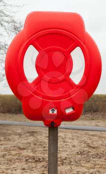 Bright red lifebuoy case on wooden pole stands on the beach