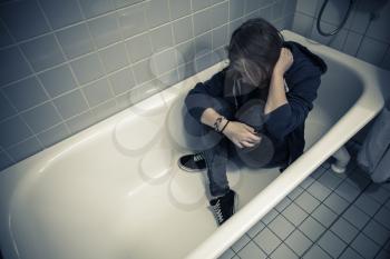 Stressed sad Caucasian teenage girl sitting in empty bath. Depression mood concept