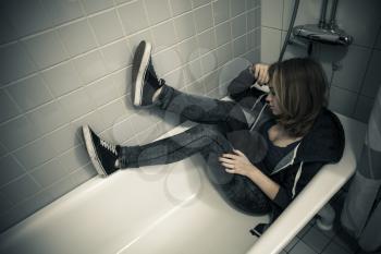 Caucasian blond teenage girl sitting in empty bath. Stylized tonal correction filter, vintage photo with old style effect