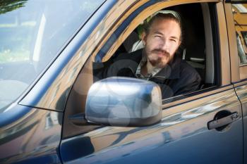Bearded serious Asian man, driver of modern Japanese crossover suv car, outdoor portrait in open car window