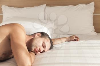 Young European man sleeping in wide bed in morning sunlight
