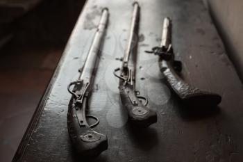 Three ancient guns lay on dark wooden table, closeup photo with selective focus