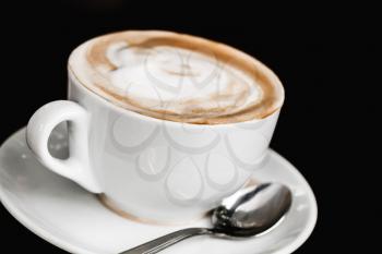 Cup of cappuccino. White mug of coffee with milk foam over black table background, closeup photo with selective focus