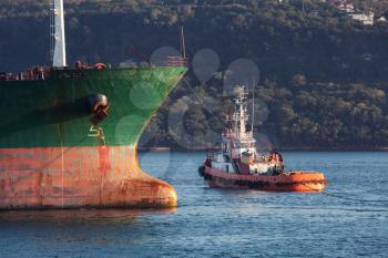 Red tug goes near bow of big cargo ship. Black sea, Varna harbor, Bulgaria