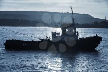 Tug boat is underway. Black sea, Varna harbor, Bulgaria. Blue toned dark silhouette photo