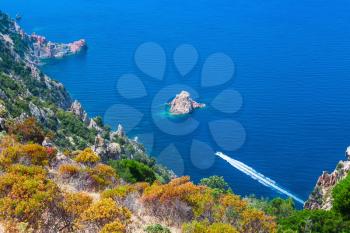 Coastal landscape of South Corsica. Fast motor boat goes along Capo Rosso, Piana region