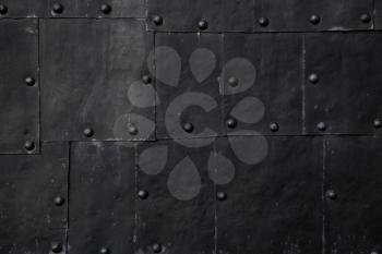 Old black submarine hull fragment, grungy metal sheets with rivets, background photo texture