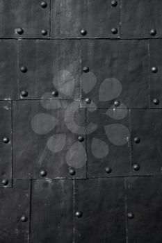 Black submarine hull fragment, grungy metal sheets with rivets, vertical background photo texture
