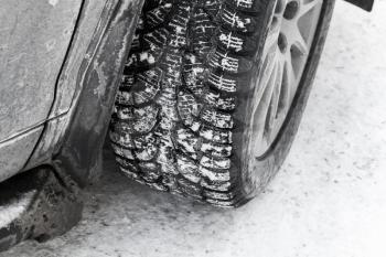 Car wheel on snow tire with metal studs, which improve traction on icy surfaces in winter season