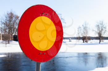 Round red and yellow stop sign mounted on winter river coast