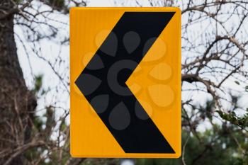 Dangerous turn left, yellow black road sign mounted on roadside
