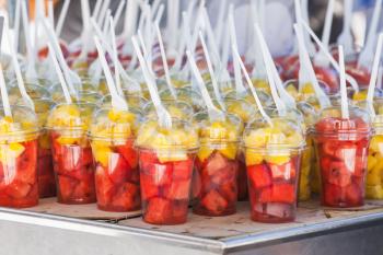 Sliced fresh fruits sorted in plastic cups with forks. Street dessert shop in Lisbon, Portugal. Close-up photo with selective focus