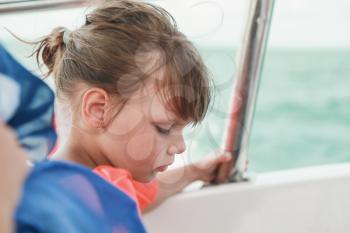 Caucasian little girl in orange life-jacket as a passenger of motorboat, close-up profile portrait