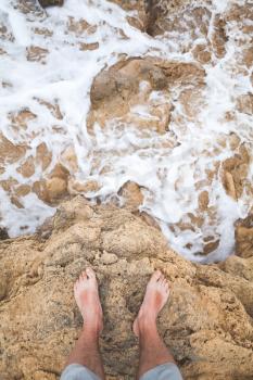 Top view of male bare feet on coastal rocks. Travel lifestyle, vertical background photo