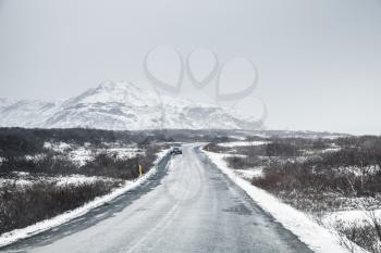 Icelandic road covered with ice and snow, rural landscape with snowy mountains on horizon