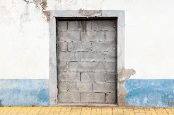 Doorway in old white wall blocked with concrete bricks
