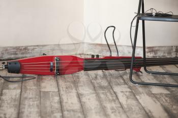 Live music background, modern electric red double bass lays on grungy wooden floor of musical studio, close-up photo with selective focus