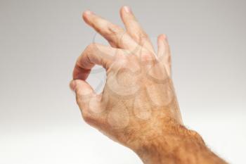 Closeup photo male hand showing Ok acceptance gesture over gray background