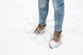 Female feet in blue jeans and high boots of nubuck standing in fresh snow, winter walking