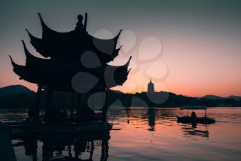 Chinese landscape at sunset, ancient gazebo pavilion and rowing boat on West Lake. Popular public park of Hangzhou city, China