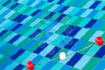 Red and white plastic floats on rope, swimming pool background
