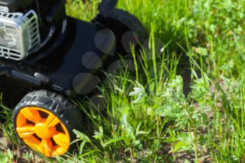 Lawn mower or grass cutter stands on green lawn, closeup photo with selective focus on grass