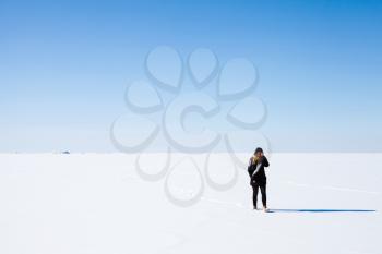 Teenage girl in black walks on frozen Baltic Sea under bright blue winter sky