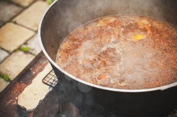 Spicy broth with lamb and vegetables boil in a cauldron. Preparing of Chorba soup on open fire, traditional meal for many national cuisines in Europe, Africa and Asia 