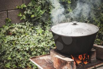 Closed black cauldron boiling on a bonfire. Outdoor preparing of Chorba soup