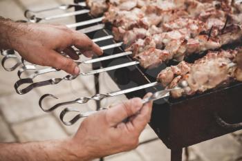 Cooking of a pork Shashlik or shashlyk, a dish of skewered and grilled cubes of meat. Cooks hands, closeup photo with selective focus 