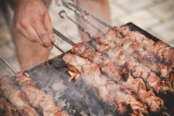 Cooking of a pork Shashlik or shashlyk, a dish of skewered and grilled cubes of meat. Cooks hand, close up photo with selective focus 