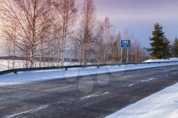 Empty rural road with information and parking signs on a roadside, winter landscape, Finland