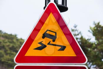 Slippery road, warning triangle road sign over bright sky background