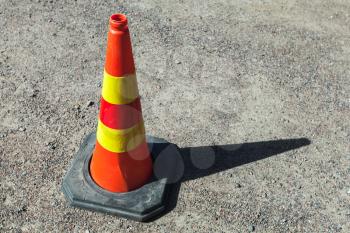Red and yellow striped warning road cone stands on urban ground