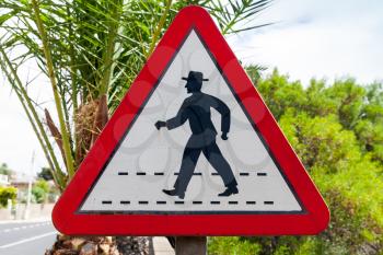 Triangle road sign with schematic walking man in hat, pedestrian zebra crossing ahead. Madeira, Portugal