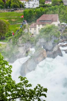 The Rhine Falls vertical landscape. Touristic viewpoint with flag on the rock in fast flowing river water