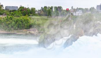 The Rhine Falls landscape. Touristic viewpoint with flag on the rock in fast flowing river water