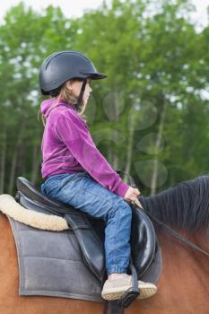 Little Caucasian girl is riding a brown horse, profile photo