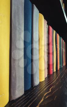 Old books in colorful covers stand in a row on wooden shelf, vertical photo