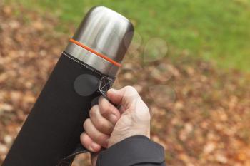 Stainless steel vacuum tourist thermos in male hand
