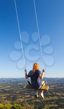 Red haired teenage girl swinging on a swing. The top of Montana Redonda. Dominican Republic