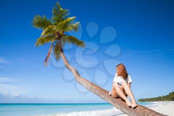 Teenage girl sitting on a palm tree. Saona island beach. Atlantic ocean coast, Dominican Republic