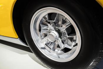 Chromed wheel disc. Yellow luxury Italian vintage sport car fragment, close up photo with selective soft focus