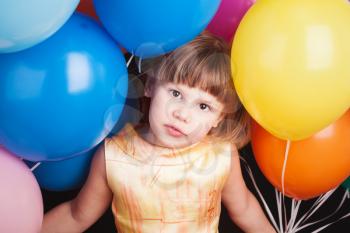 Portrait of little Caucasian blond girl with colorful balloons over black background