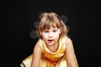 Studio portrait of little Caucasian blond girl in yellow dress on black background