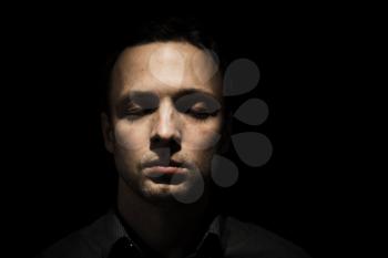 Closeup studio face portrait of young adult European man with closed eyes isolated over black background, low key photo