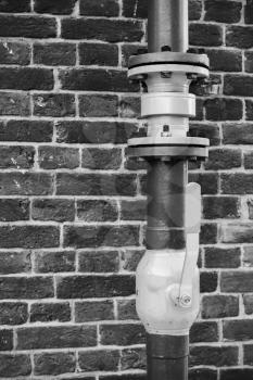 Gas tubing with open valve above brick wall, black and white photo