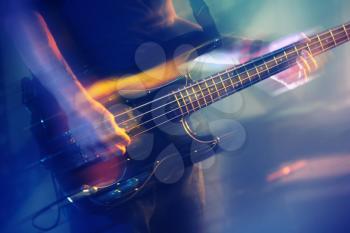 Colorful blurred rock music background, bass guitar player on a stage with colorful illumination