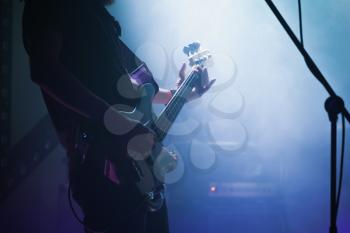 Live rock music background, electric bass guitar player in blue smoke, closeup photo with soft selective focus
